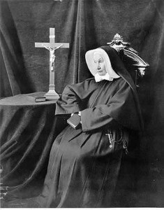 Mehegan in a nun's garb, sitting next to a cross