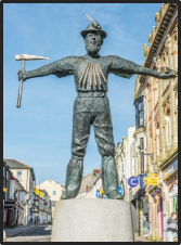 Statue of a Redruth village miner, wearing a hat and holding a pick.