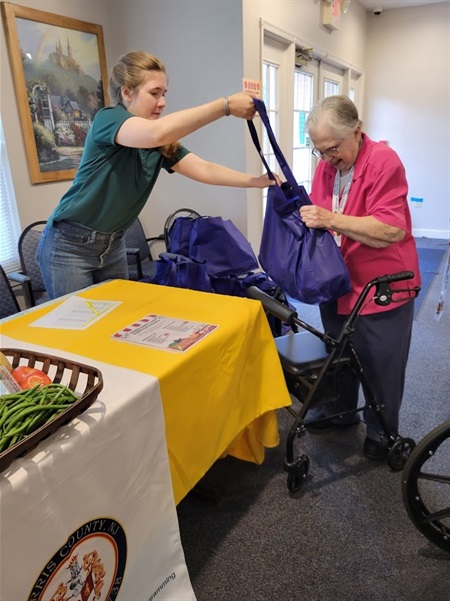 Nutrition Program summer intern Melinda Reed passes a produce bag to a senior resident 