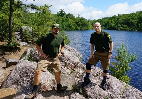 Two rangers standing on a rock with a lake in the background