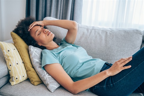 Woman looking stressed, hand on her forehead, lying on a couch