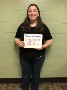 Catrina Bennett holds up a sign saying Despite my diagnosis, I refuse to be a statistic