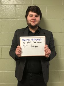 Matthew Bristol holding a sign saying Despite my diagnosis, I still find ways to laugh.