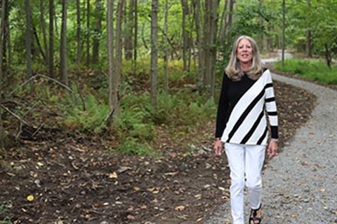 Commissioner Deb Smith, a tall blonde woman, walking down a nature path with the woods behind her.
