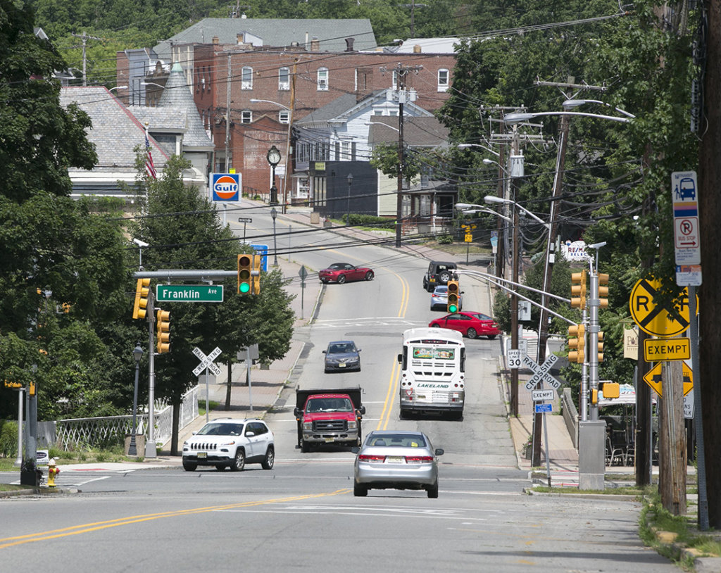 Photo looking downhill into a downtown main street with cars, trucks buses, and railroad track.