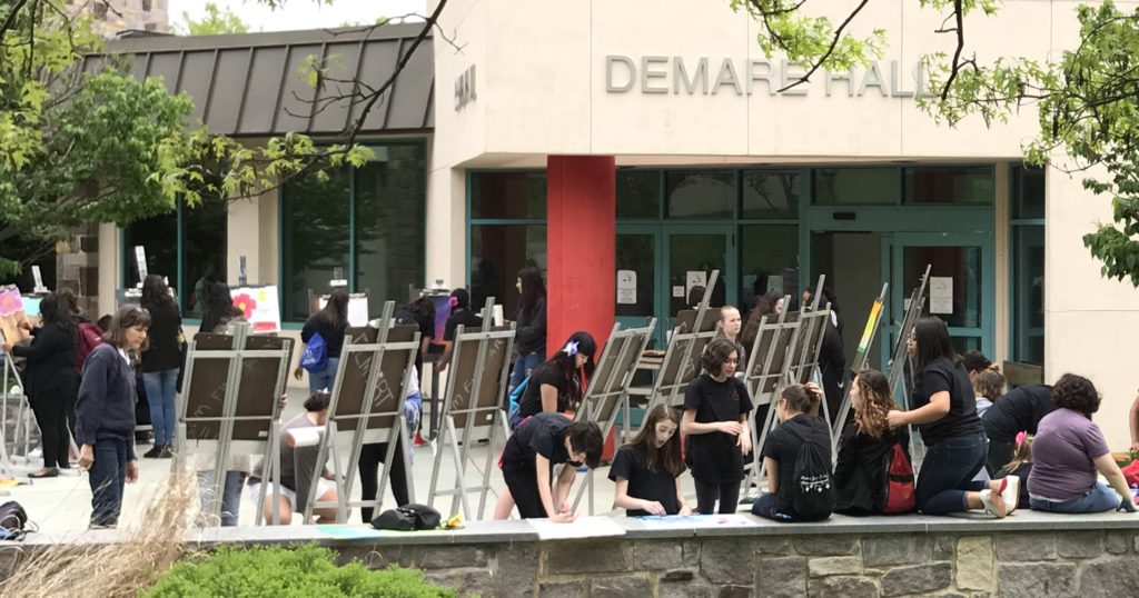 Students prepare to work at easels on the patio of DeMare Hall