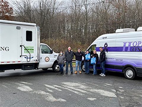 Group of Hope One and Hope Hub workers smiling in front of the two vans